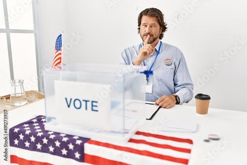 Handsome middle age man sitting at voting stand asking to be quiet with finger on lips. silence and secret concept. photo