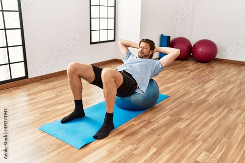 Middle age caucasian man training using fit ball at sport center