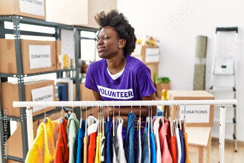African young woman wearing volunteer t shirt at donations stand with hand on stomach because nausea, painful disease feeling unwell. ache concept.
