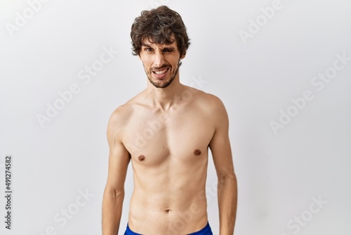 Young hispanic man standing shirtless over isolated, background winking looking at the camera with sexy expression, cheerful and happy face.
