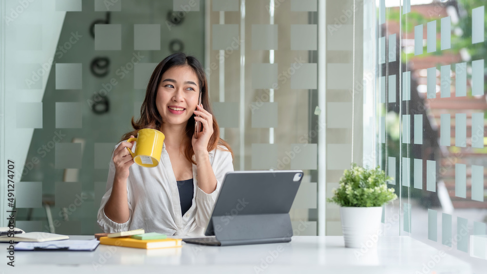 Smiling young Asian businesswoman sitting talking on the phone with laptop computer on desk in the office. Smiling young Asian businesswoman sitting talking on the phone with laptop computer on desk in the office.