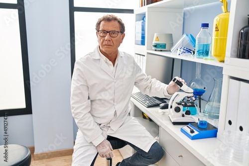 Senior man working at scientist laboratory thinking attitude and sober expression looking self confident