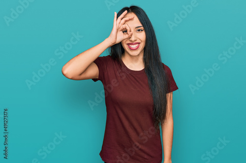 Young hispanic girl wearing casual t shirt doing ok gesture with hand smiling, eye looking through fingers with happy face. © Krakenimages.com