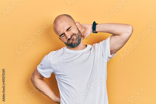 Young bald man wearing casual white t shirt suffering of neck ache injury, touching neck with hand, muscular pain