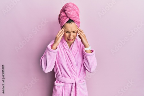 Young blonde woman wearing shower towel cap and bathrobe with hand on head, headache because stress. suffering migraine. © Krakenimages.com