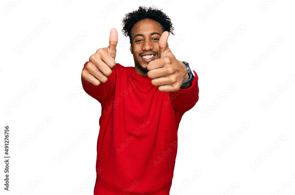 Young african american man with beard wearing casual winter sweater approving doing positive gesture with hand, thumbs up smiling and happy for success. winner gesture. Young african american man with beard wearing casual winter sweater approving doing positive gesture with hand, thumbs up smiling and happy for success. winner gesture.