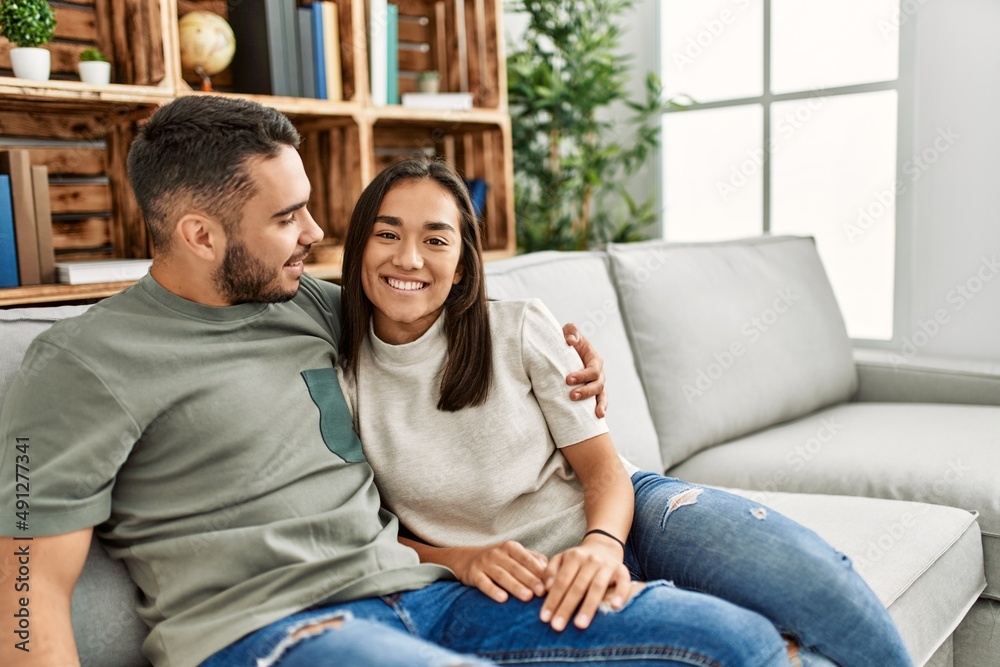 Fototapeta premium Young latin couple sitting on the sofa hugging at home.