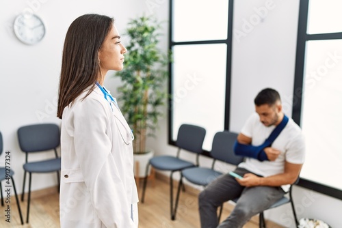 Young asian doctor woman at waiting room with a man with a broken arm looking to side, relax profile pose with natural face with confident smile.