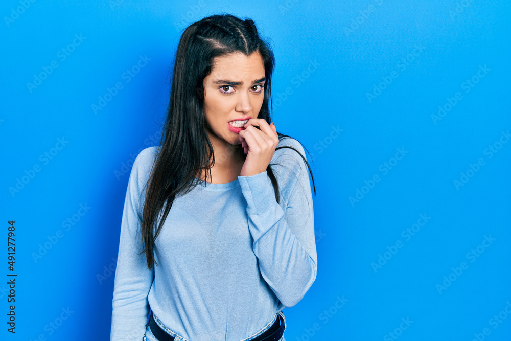 Young hispanic girl wearing casual clothes looking stressed and nervous with hands on mouth biting nails. anxiety problem. Young hispanic girl wearing casual clothes looking stressed and nervous with hands on mouth biting nails. anxiety problem.