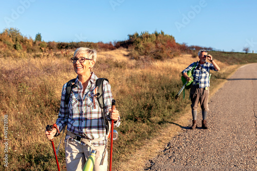 Mature woman walk while man standing behind in background and looking through binoculars