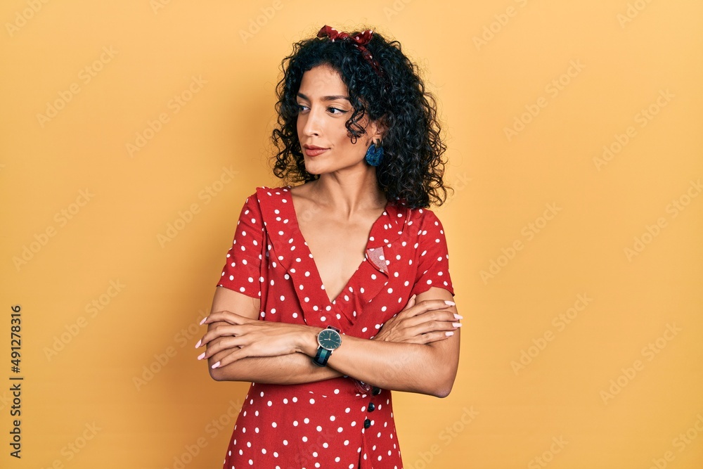 Young latin girl wearing summer dress looking to the side with arms crossed convinced and confident Young latin girl wearing summer dress looking to the side with arms crossed convinced and confident