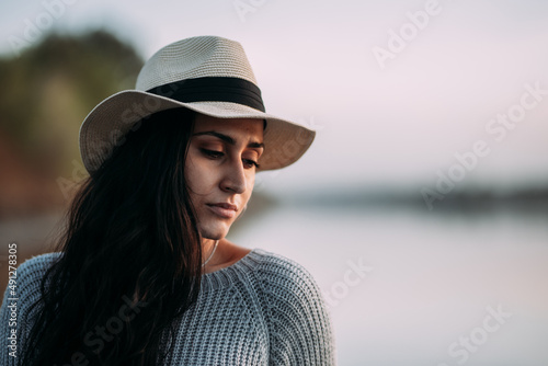 Horizontal portrait of a pensive and serious woman with her eyes closed wearing a hat by a lake © antoniosantosc