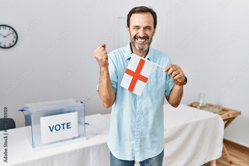 Middle age man with beard at political campaign election holding england flag screaming proud, celebrating victory and success very excited with raised arm