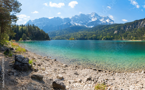rocky bathing beach at lake shore Eibsee, view to Zugspitze mountain, upper bavaria in spring