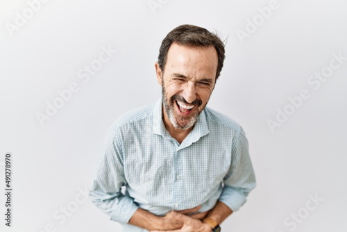 Middle age hispanic man with beard standing over isolated background smiling and laughing hard out loud because funny crazy joke with hands on body.