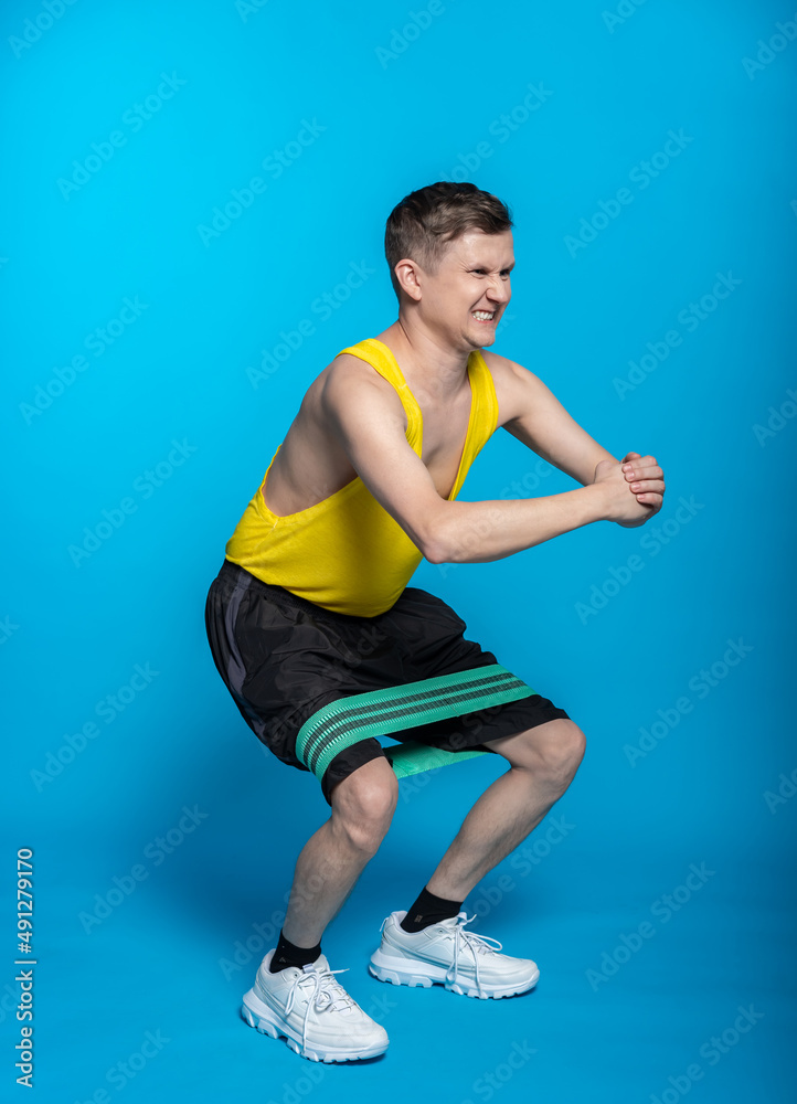 thin athlete in a yellow t-shirt and black shorts on a blue background. funny shakes muscles, goes in for sports, fitness