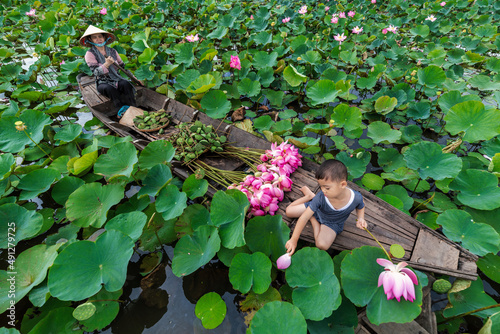 Top view of vietnamese boy playing with mom over the traditional wooden boat when padding for keep the pink lotus in the big lake at thap muoi, dong thap province, vietnam, culture and life concept photo