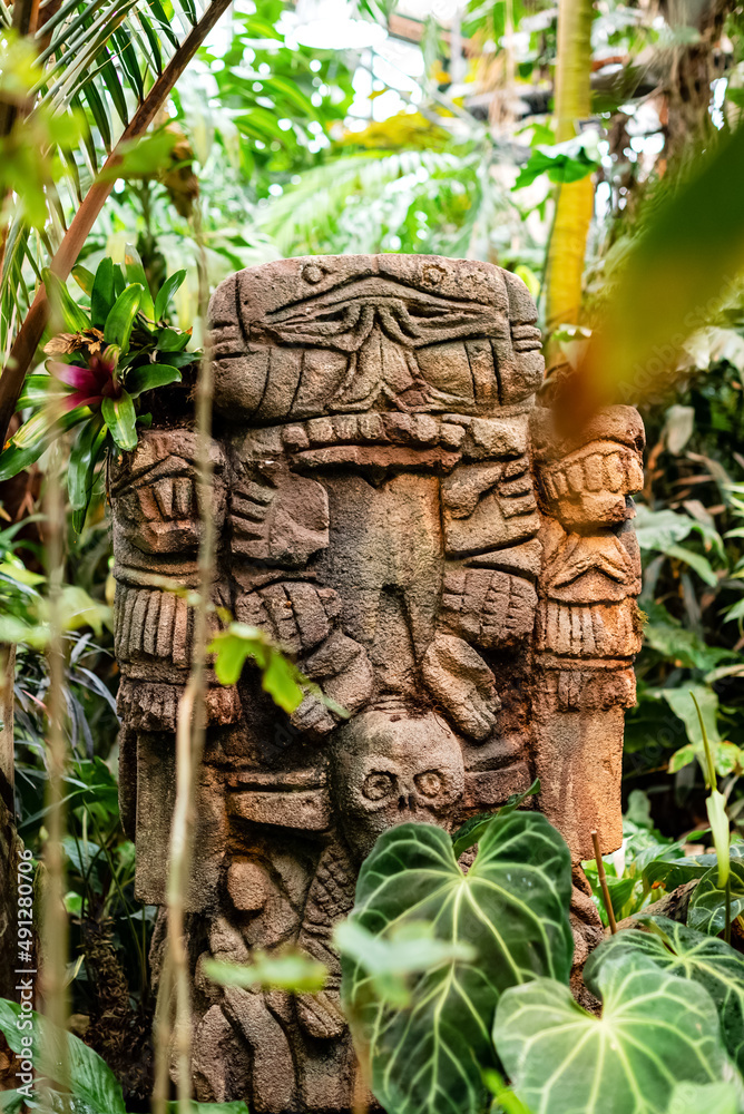 Obraz premium Stone carved totem with human face among tropical plants