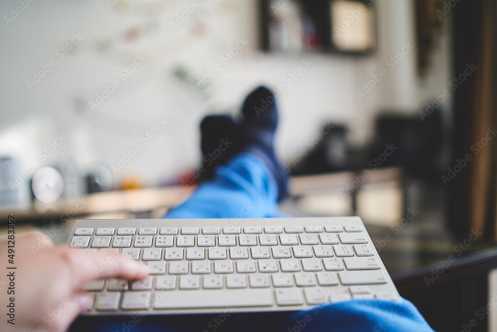 Hands on the keyboard from the computer on a blurred background of the apartment and men's feet Hands on the keyboard from the computer on a blurred background of the apartment and men's feet
