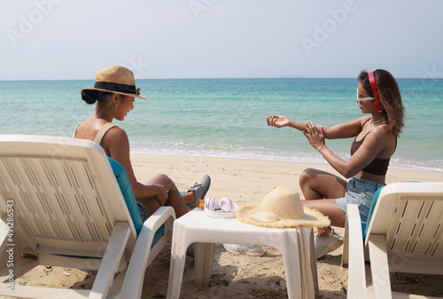 summer holidays and vacation -Two asia womem tourist applying sun protection cream on the beachsite , Happy women with sunbating on tropical beach photo