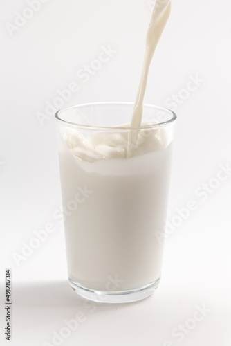 Milk is poured into a transparent glass on a white background