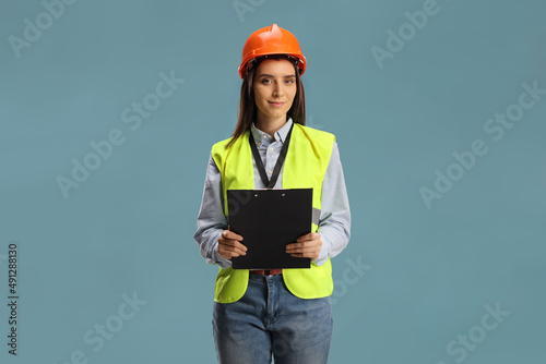 Young female engineer with a safety vest and hardhat holding a clipboard photo