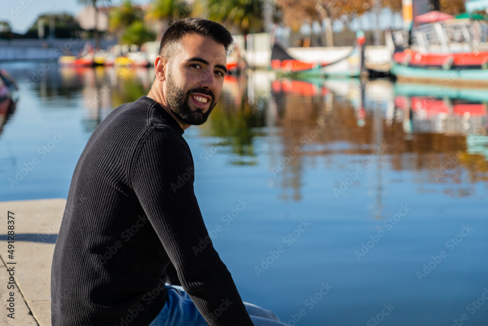 Handsome man with beard sitting on the canals of Aveiro on a sunny day, Portugal