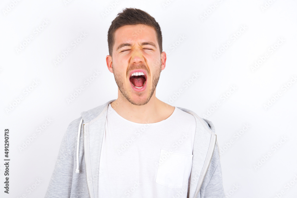Stressful young caucasian man wearing casual clothes over white background screams in panic, closes eyes in terror, keeps hands on head, finds out terrified news, can't believe it. Stressful young caucasian man wearing casual clothes over white background screams in panic, closes eyes in terror, keeps hands on head, finds out terrified news, can't believe it.