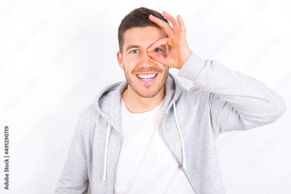 young caucasian man wearing casual clothes over white background with happy face smiling doing ok sign with hand on eye looking through finger.