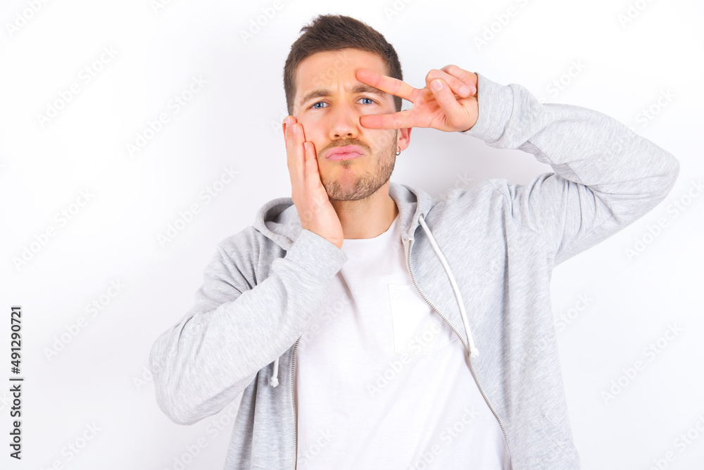 young caucasian man wearing casual clothes over white background making v-sign near eyes. Leisure lifestyle people person celebrate flirt coquettish concept. young caucasian man wearing casual clothes over white background making v-sign near eyes. Leisure lifestyle people person celebrate flirt coquettish concept.