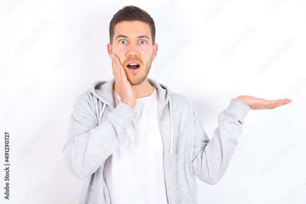 Positive glad young caucasian man wearing casual clothes over white background says: wow how exciting it is, indicates something. One hand on his head and pointing with other hand. Positive glad young caucasian man wearing casual clothes over white background says: wow how exciting it is, indicates something. One hand on his head and pointing with other hand.