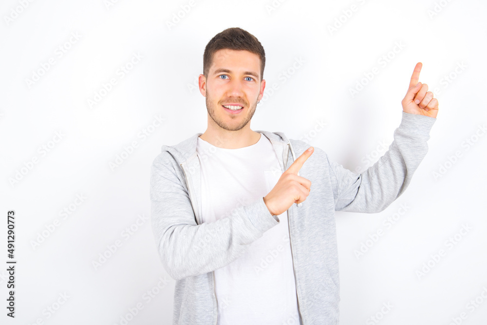 Positive young caucasian man wearing casual clothes over white background with beaming smile pointing with two fingers and looking on empty copy space. Advertisement concept. Positive young caucasian man wearing casual clothes over white background with beaming smile pointing with two fingers and looking on empty copy space. Advertisement concept.