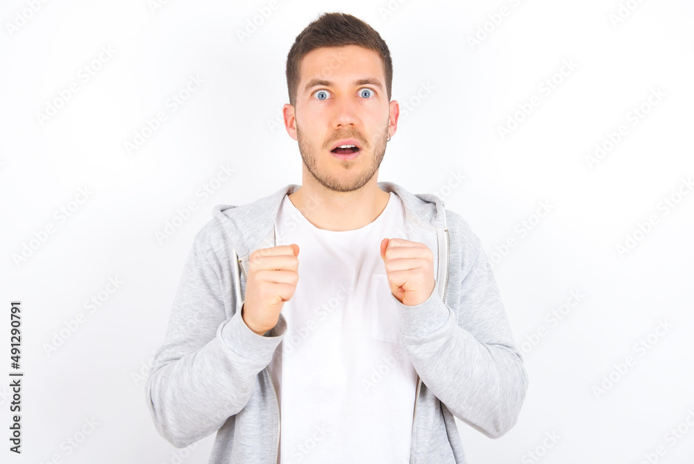 Portrait of desperate and shocked young caucasian man wearing casual clothes over white background looking panic, holding hands near face, with mouth wide open. Portrait of desperate and shocked young caucasian man wearing casual clothes over white background looking panic, holding hands near face, with mouth wide open.