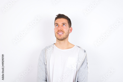 Portrait of mysterious young caucasian man wearing casual clothes over white background looking up with enigmatic smile. Advertisement concept. © Jihan