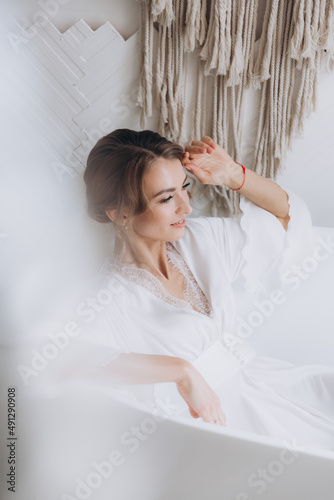 Morning of the bride in a rustic style, in a white bathrobe and a white bouquet on the bed and in the bathroom by the window in a photo studio, in a hotel