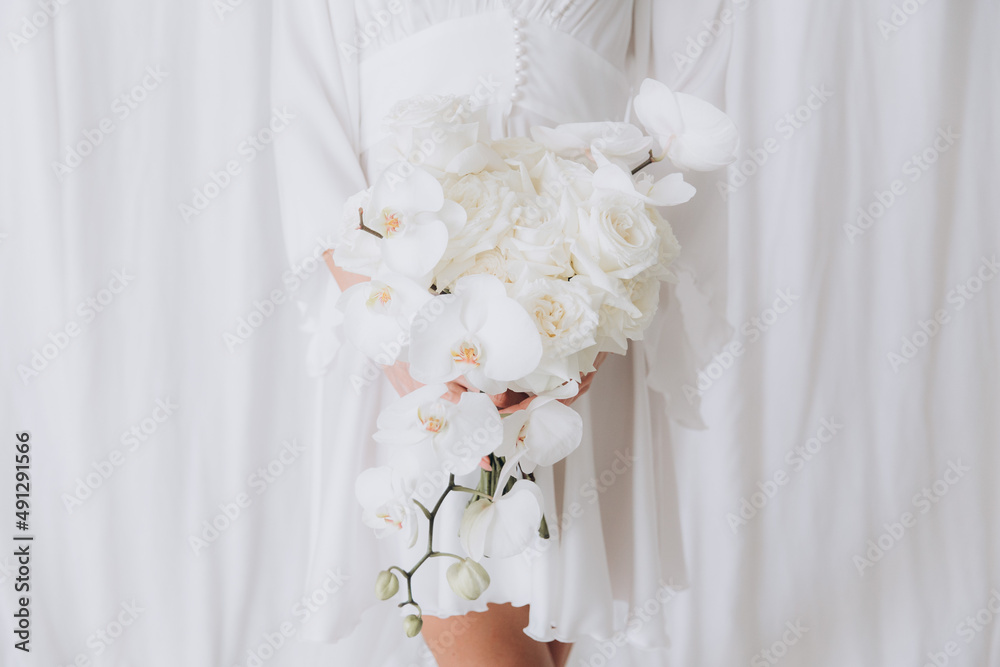 Morning of the bride in a rustic style, in a white bathrobe and a white bouquet on the bed and in the bathroom by the window in a photo studio, in a hotel