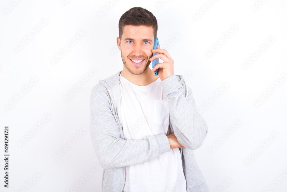 Portrait of a smiling young caucasian man wearing casual clothes over white background talking on mobile phone. Business, confidence and communication concept. Portrait of a smiling young caucasian man wearing casual clothes over white background talking on mobile phone. Business, confidence and communication concept.