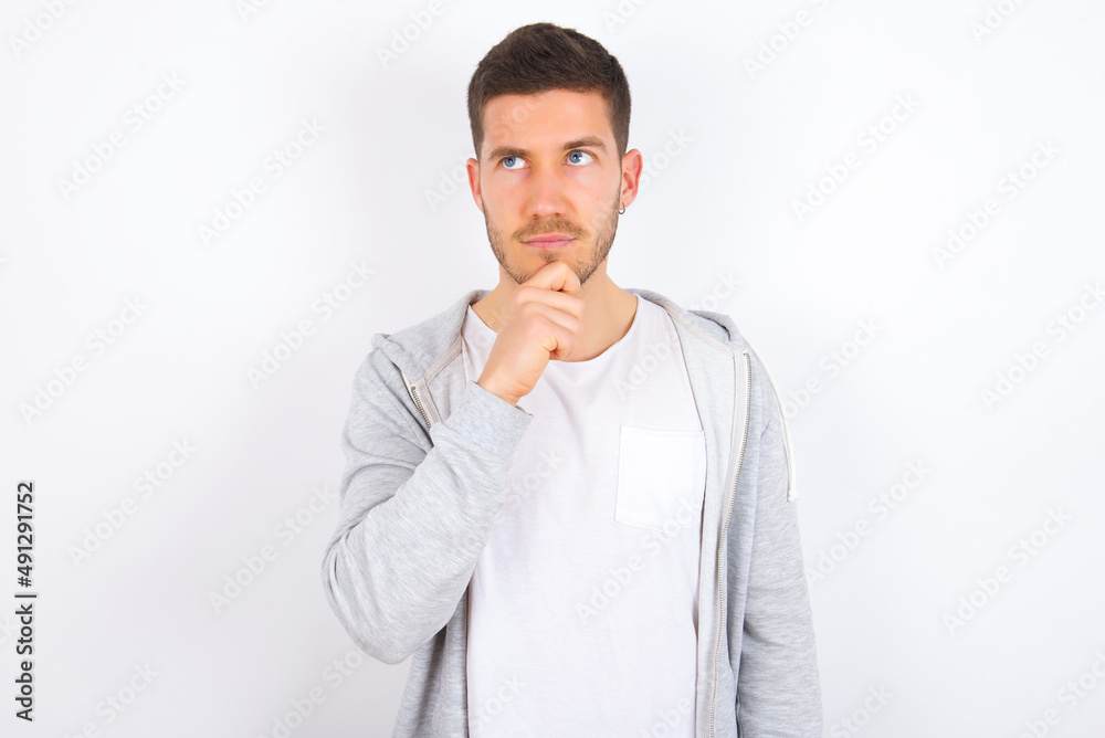 Thoughtful young caucasian man wearing casual clothes over white background holds chin and looks away pensively makes up great plan Thoughtful young caucasian man wearing casual clothes over white background holds chin and looks away pensively makes up great plan