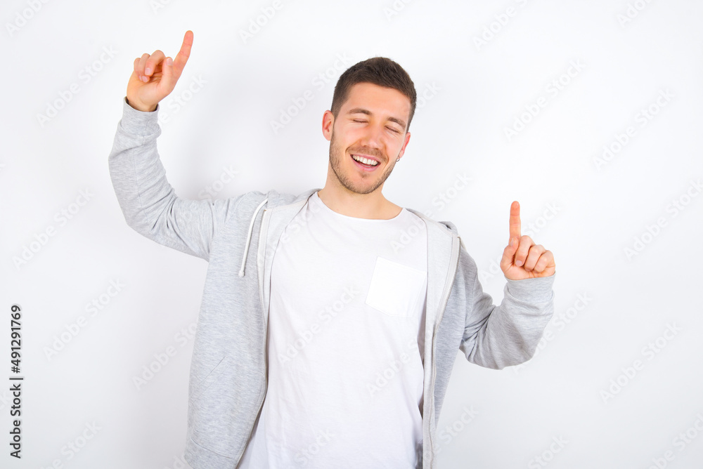 Photo of upbeat young caucasian man wearing casual clothes over white background has fun and dances carefree wear being in perfect mood makes movements. Spends free time on disco party Photo of upbeat young caucasian man wearing casual clothes over white background has fun and dances carefree wear being in perfect mood makes movements. Spends free time on disco party
