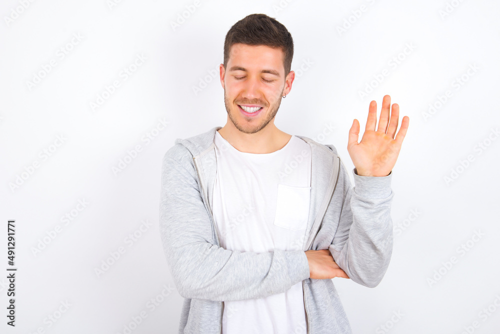Overjoyed successful young caucasian man wearing casual clothes over white background raises palm and closes eyes in joy being entertained by friends Overjoyed successful young caucasian man wearing casual clothes over white background raises palm and closes eyes in joy being entertained by friends