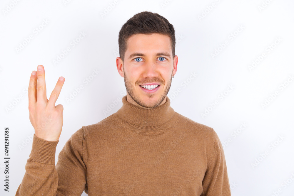 young caucasian man wearing knitted turtleneck over white background smiling and looking friendly, showing number three or third with hand forward, counting down