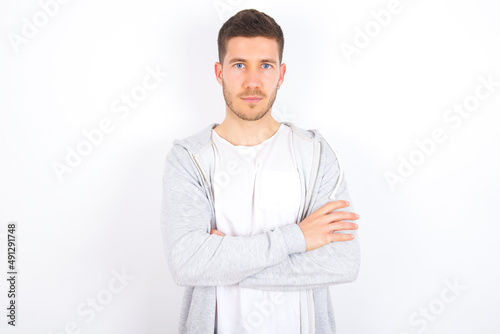 Self confident serious calm young caucasian man wearing casual clothes over white background  stands with arms folded. Shows professional vibe stands in assertive pose.