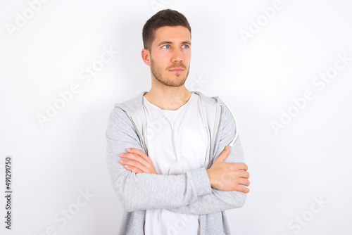 Charming thoughtful young caucasian man wearing casual clothes over white background stands with arms folded concentrated somewhere with pensive expression thinks what to do