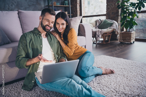 Portrait of beautiful handsome cheerful couple sitting on carpet using laptop choosing goods at home house flat indoors photo