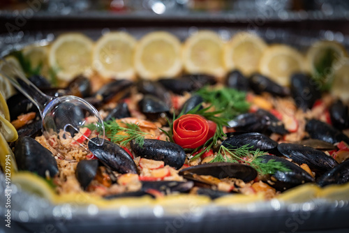 Seafood, seashells, mussels and fake crab meat rice dish decorated with lemon slices and herbs served in the catering settings of an event