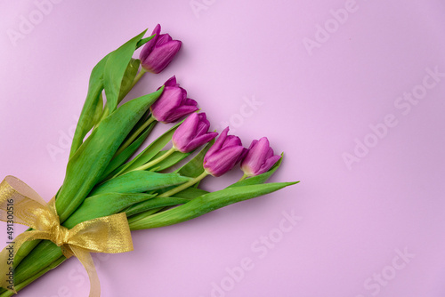 Fototapeta Naklejka Na Ścianę i Meble -  Bouquet of purple tulips with a golden ribbon on a purple background. Mother's Day, Easter, Valentine's Day. Spring flowers. Copy space. View from above.