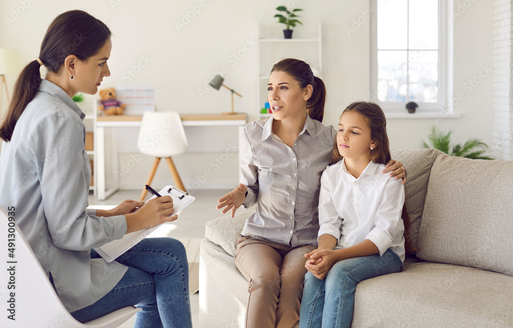 Mother sitting on sofa with sad preteen kid and talking to counseling therapist. Parent and psychologist discuss behaviour problem, peer interaction issue, ways to support child in difficult situation Mother sitting on sofa with sad preteen kid and talking to counseling therapist. Parent and psychologist discuss behaviour problem, peer interaction issue, ways to support child in difficult situation