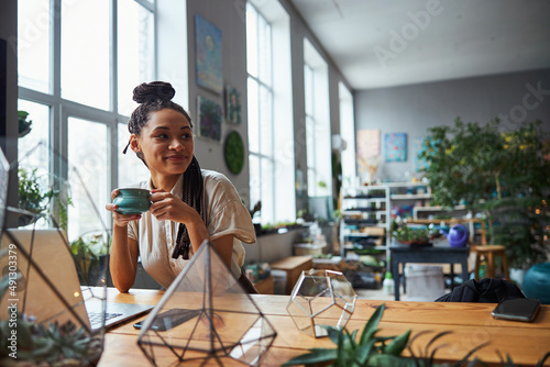 фотографія Pleased florist with cornrows daydreaming during the tea break