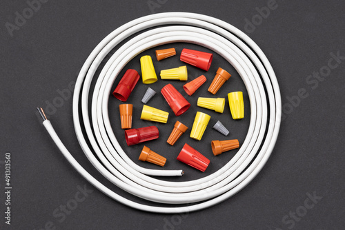 Horizontal flat layout of assorted color wire nuts encircled by white electrical wire on black background photo