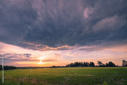 Dramatic stormy clouds over agriculture sunset summer field.